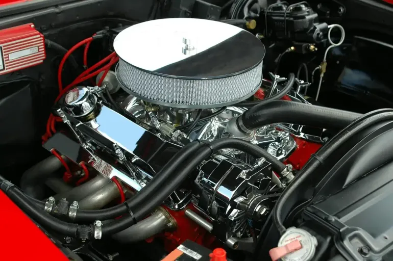 Primer plano de un motor V8 de automóvil pulido y pintado de rojo, con un filtro de aire cromado y tapas de válvulas, dentro de un compartimento del motor abierto.