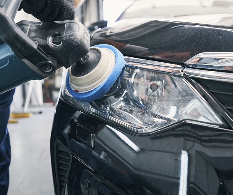 Una persona está puliendo el faro de un coche con una máquina.