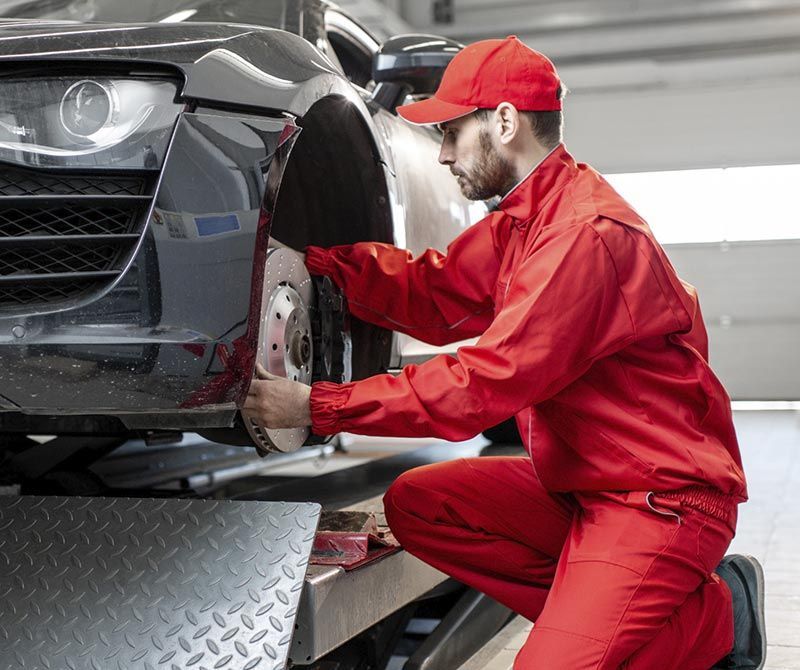 Un hombre con uniforme rojo está trabajando en un coche en un garaje.