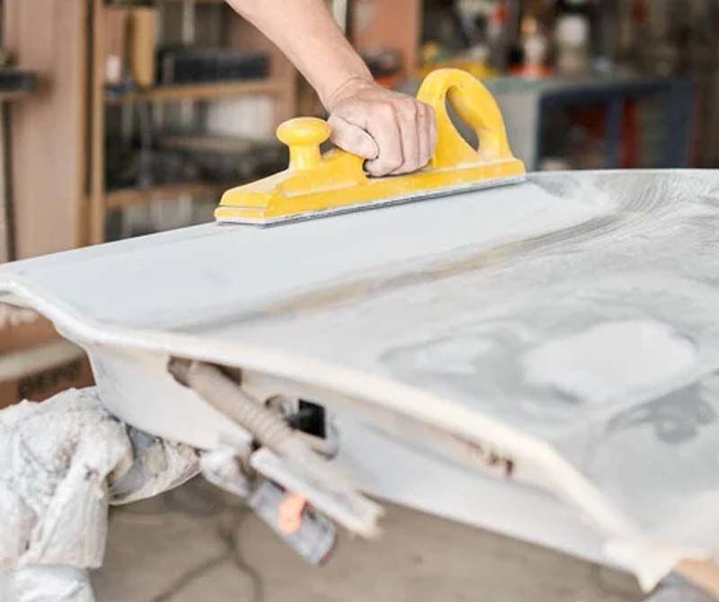 Una persona está usando un cepillo amarillo para lijar un trozo de madera.