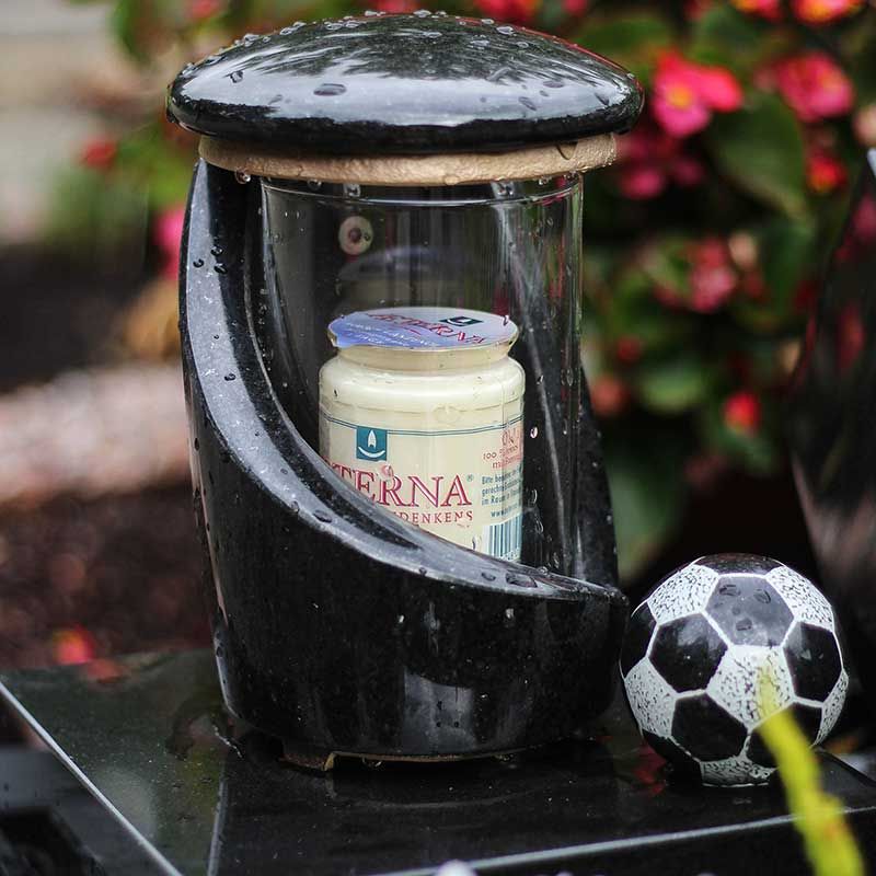 Schwarze Gedenklaterne mit einer Kerze im Inneren und einem daneben stehenden Fußball.