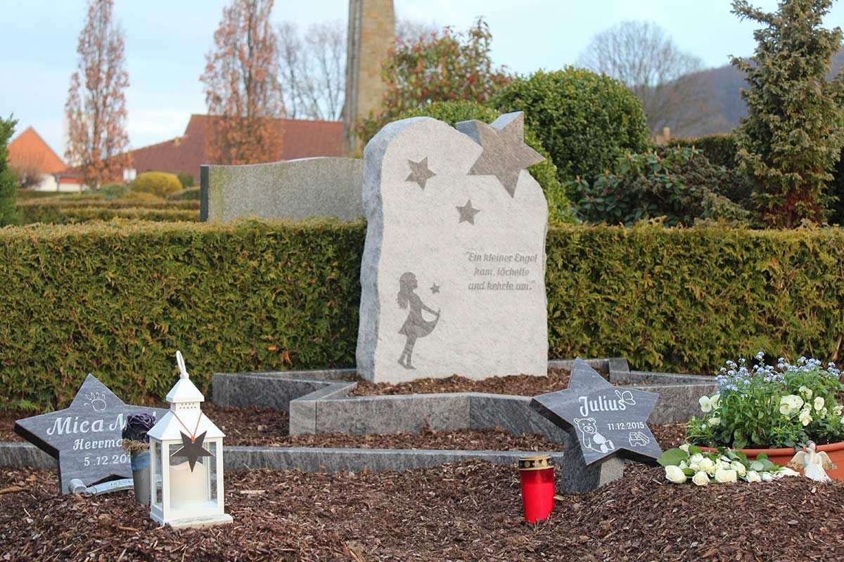 Grabmal mit sternförmigen Steinen und einem zentralen Stein mit der Silhouette eines Mädchens und eingraviertem Text, aufgestellt auf einem Friedhof.
