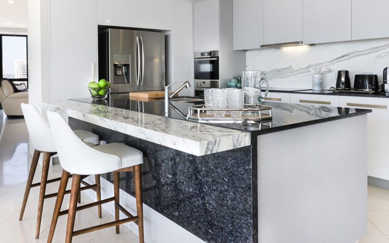 Moderne Küche mit weißen Schränken, Marmorinsel, Edelstahlgeräten und weißen Barhockern.