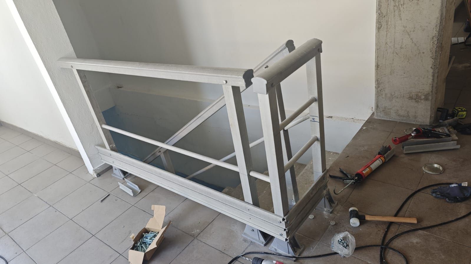 Un marco de barandilla de metal blanco parcialmente construido contra una pared blanca, con herramientas cerca en el piso.