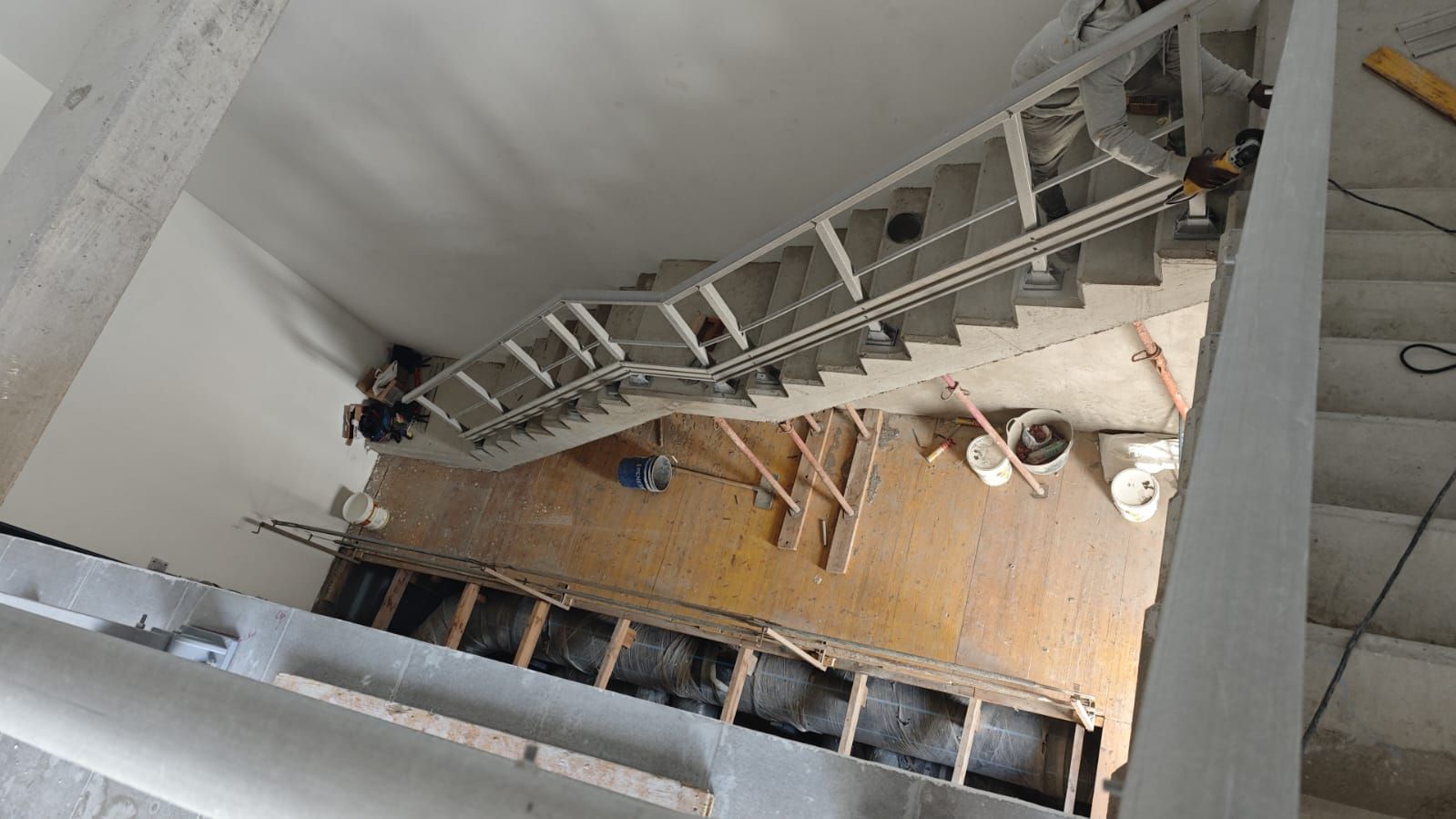 Escalera en construcción, vista desde arriba. Escalones de hormigón y paredes sin terminar con la estructura visible.