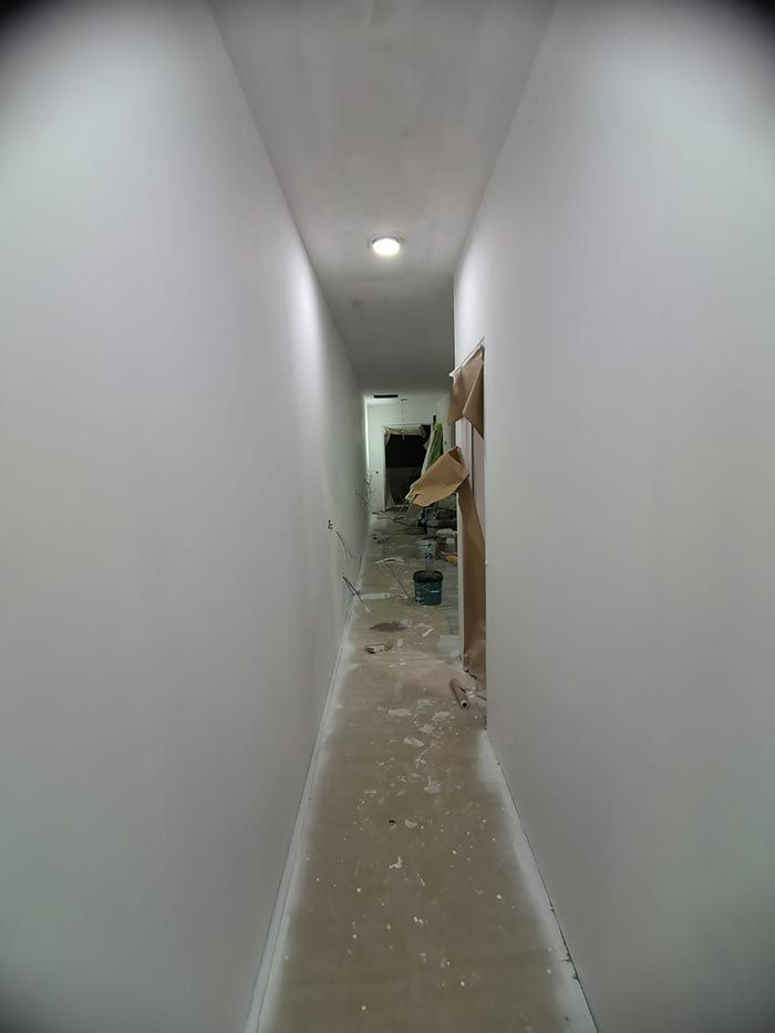 Pasillo estrecho recién pintado con una puerta al final, herramientas de construcción y escombros en el suelo.
