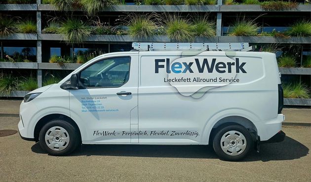 Ein Arbeiter verlegt weisse Wandfliesen in einem Badezimmer; die Aufnahme zeigt ihn von hinten; Werkzeug steht auf der Arbeitsfläche.