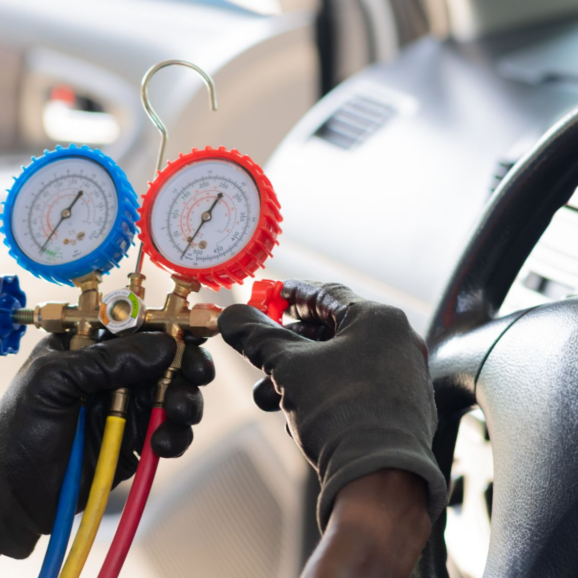 Des mains gantées de noir fixent des manomètres au système de climatisation d'une voiture en vue de sa réparation.