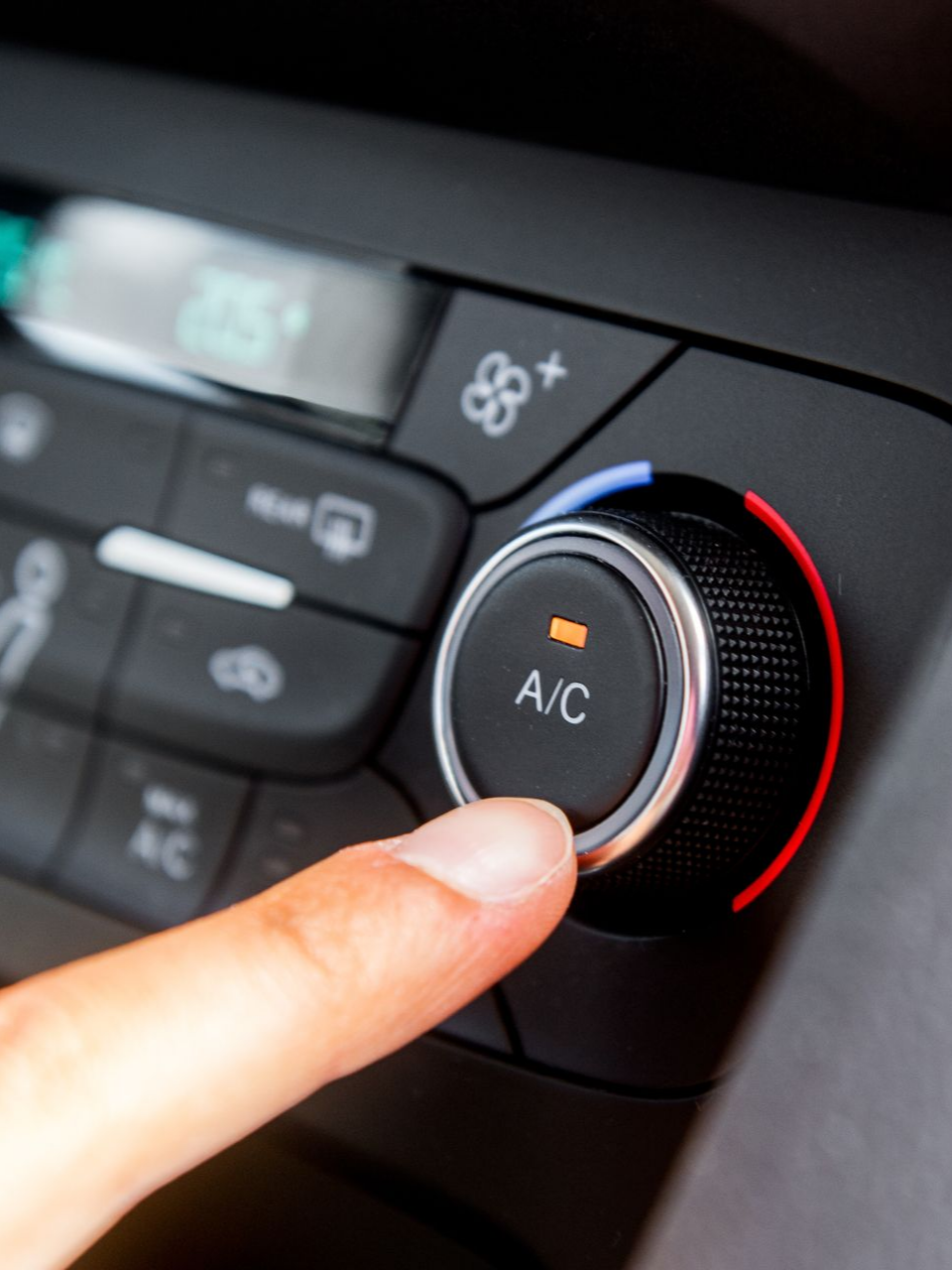 Un doigt appuie sur le bouton de climatisation du tableau de bord d'une voiture. Commandes noires et argentées avec molette de température rouge et bleue.