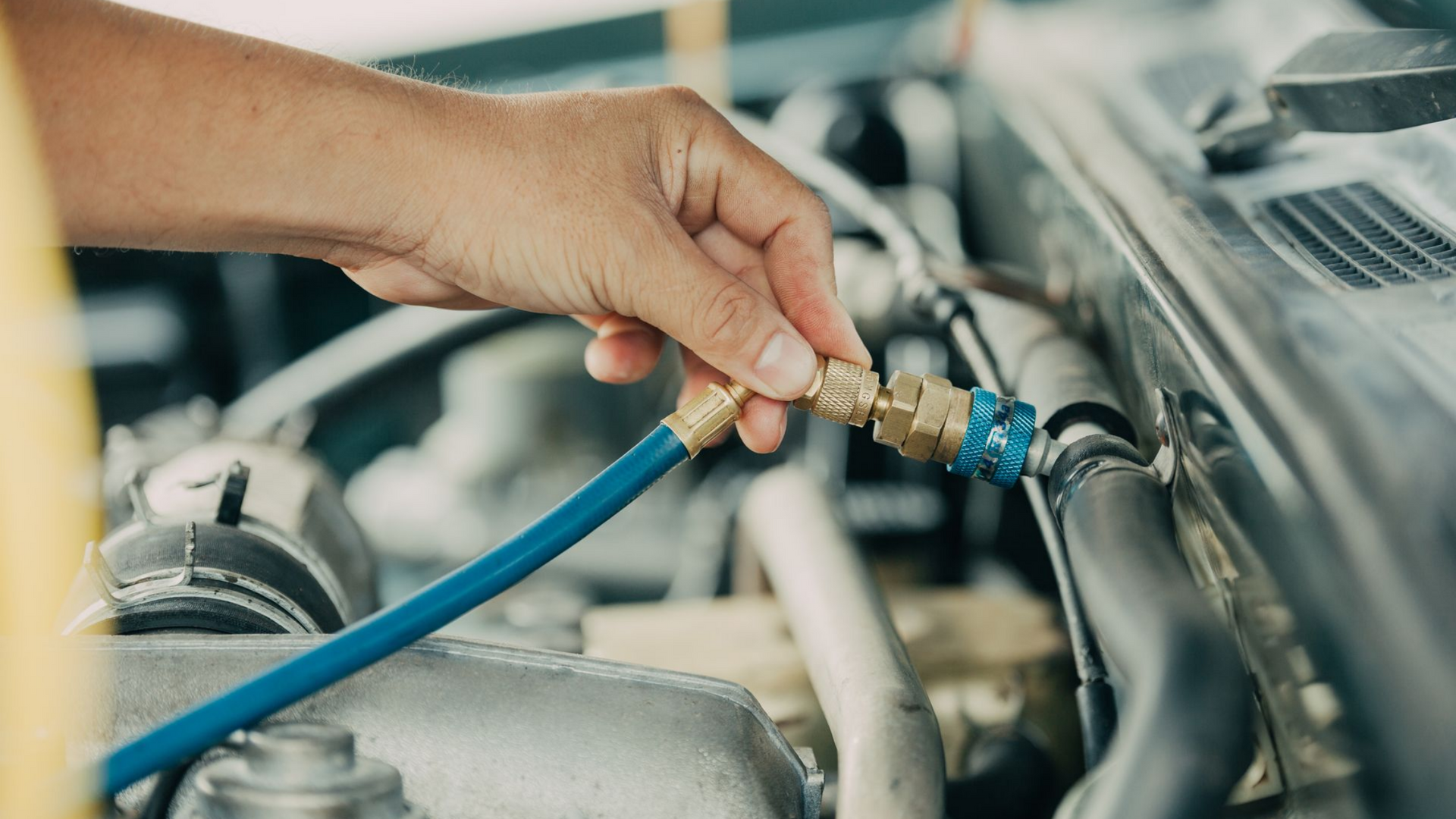 Raccordement manuel d'un tuyau bleu à un composant du système de climatisation automobile dans le compartiment moteur.