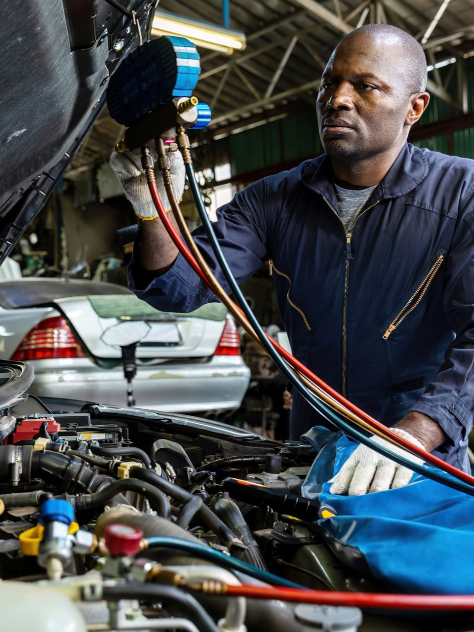 Un mécanicien en combinaison bleue vérifie le moteur d'une voiture à l'aide de jauges dans un garage.