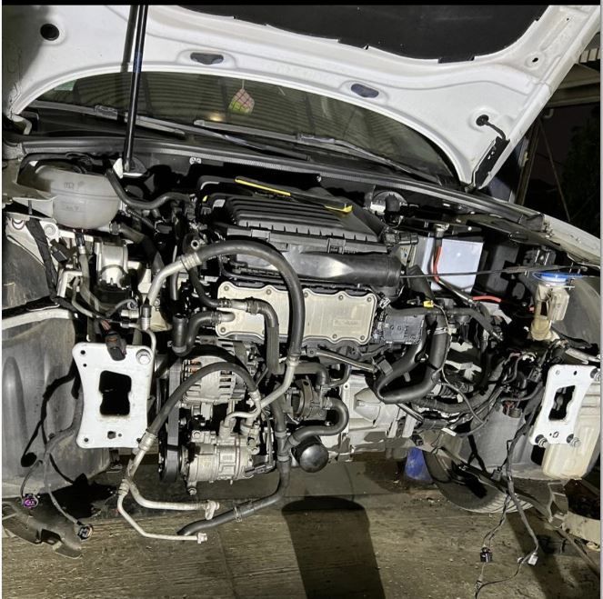 Une main gantée tient une lumière bleue près de pièces automobiles. La lumière éclaire des marquages ​​verts sur des tuyaux.