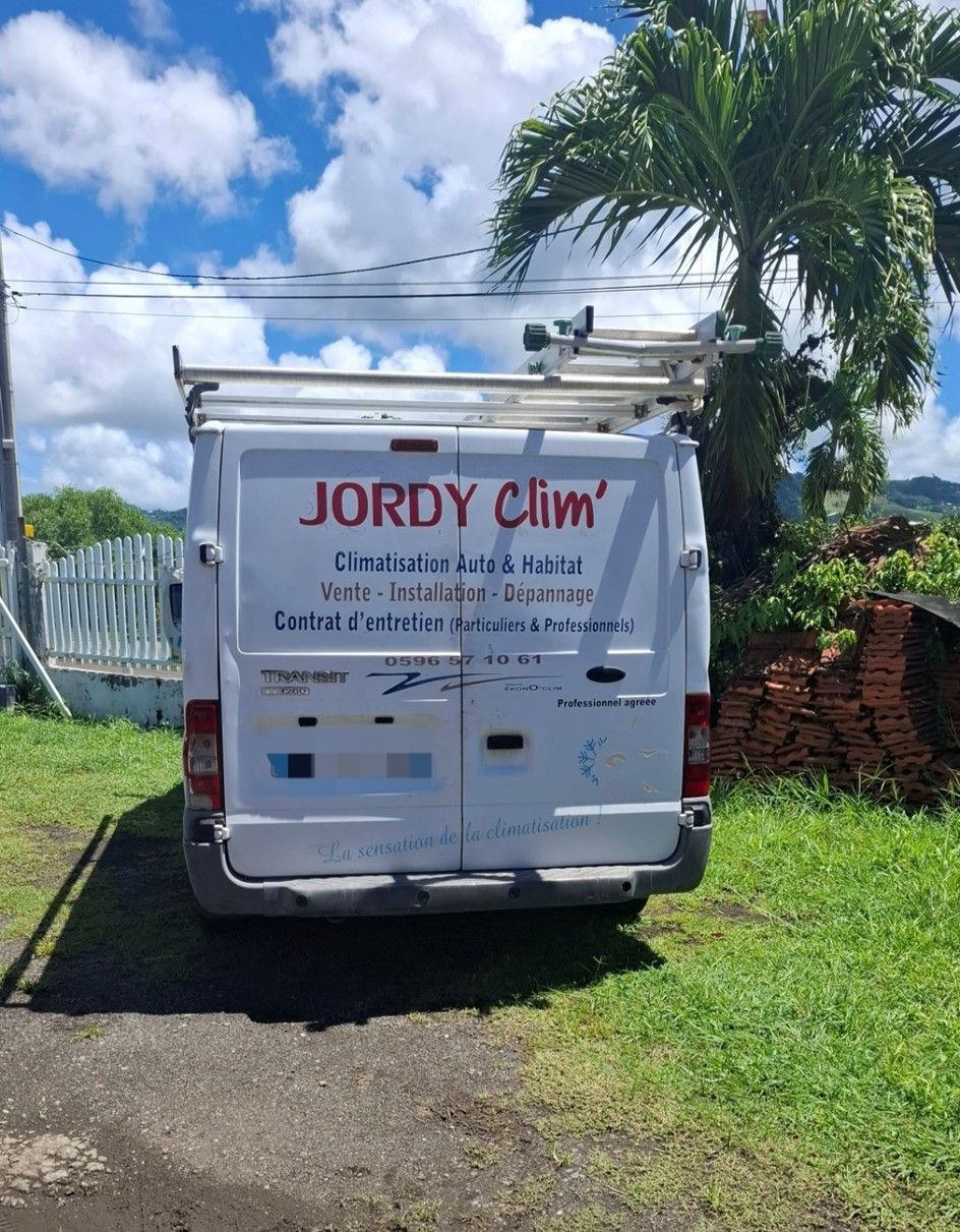 Camionnette blanche avec le logo de JORDY Clim, garée à l'extérieur avec une échelle sur le toit.