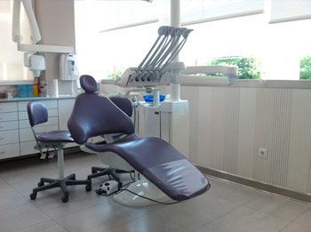 Una silla dental de color morado se encuentra en un consultorio dental junto a una ventana.