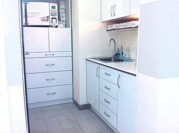 Una cocina con gabinetes blancos, cajones, un fregadero y un refrigerador.