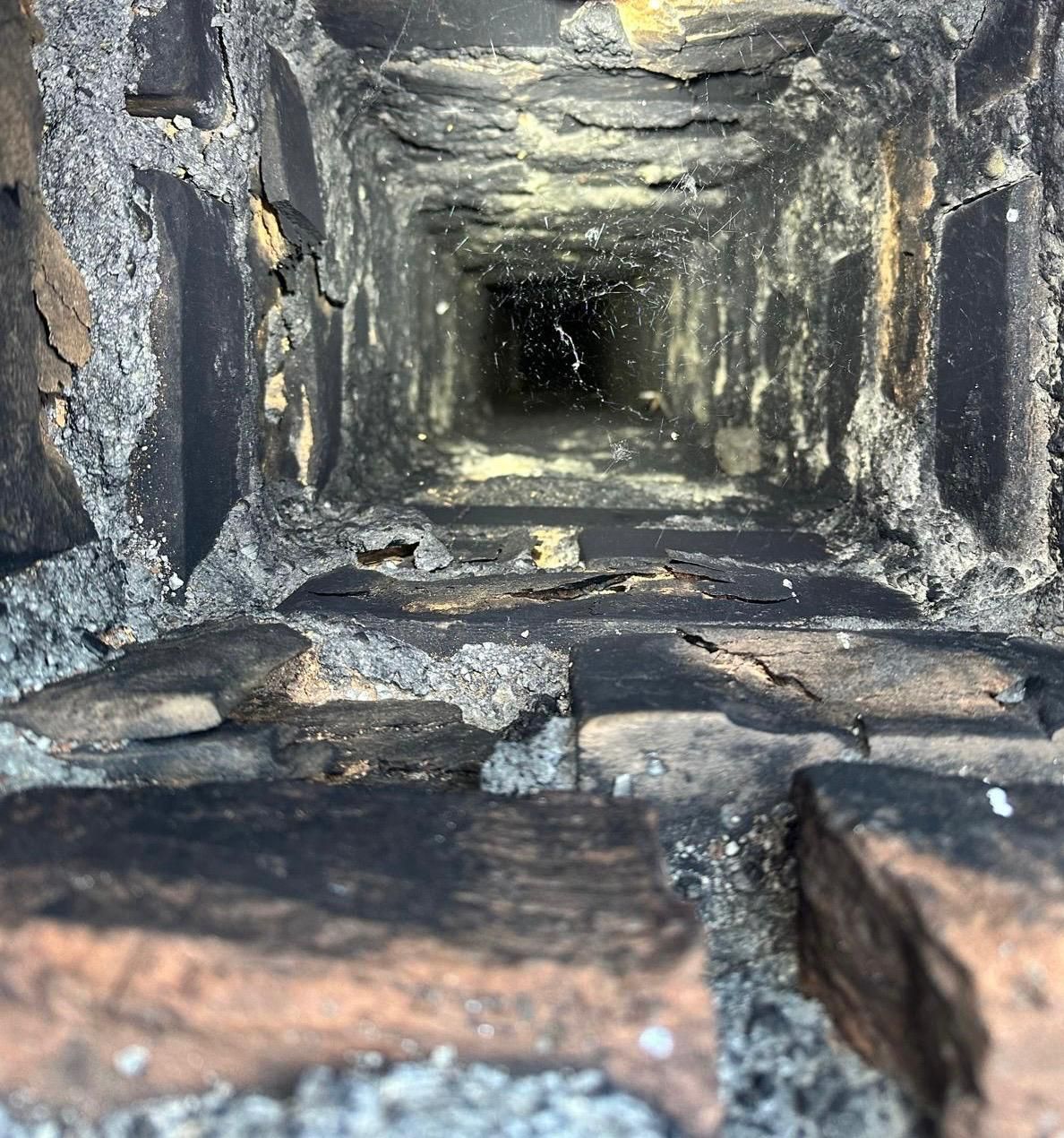 Nahaufnahme mit Blick in einen dunklen, schmalen Steinkamin oder Lüftungsschacht mit rußbefleckten Wänden.