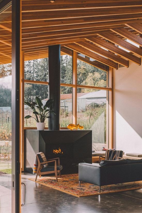 Modernes Wohnzimmer mit Kamin, hohen Fenstern, Holzdecke, dunklem Sofa und Teppich.