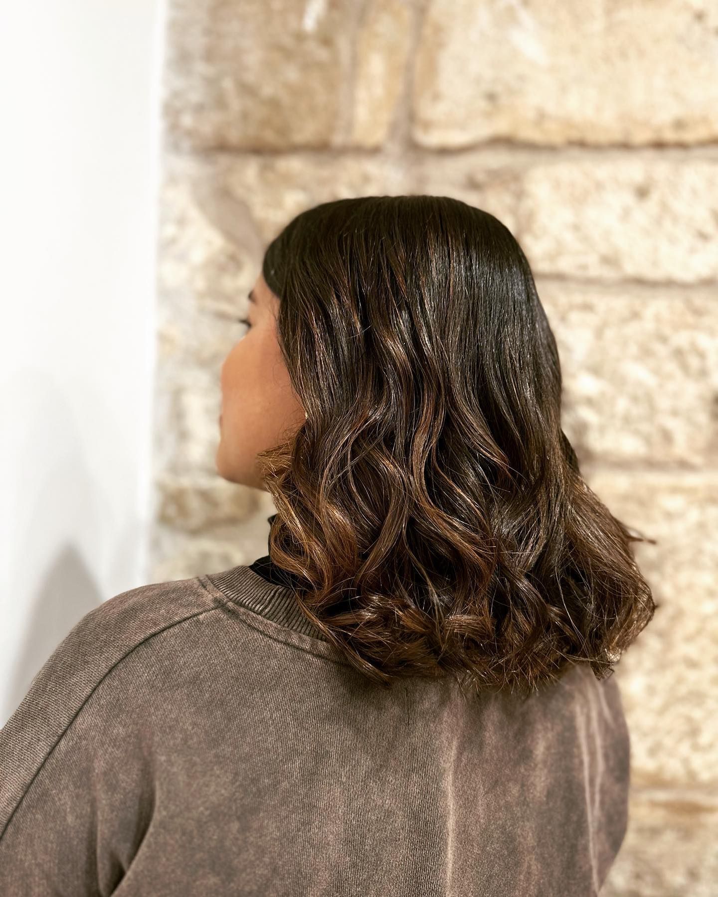 Una mujer con cabello largo y castaño está parada frente a un muro de piedra.