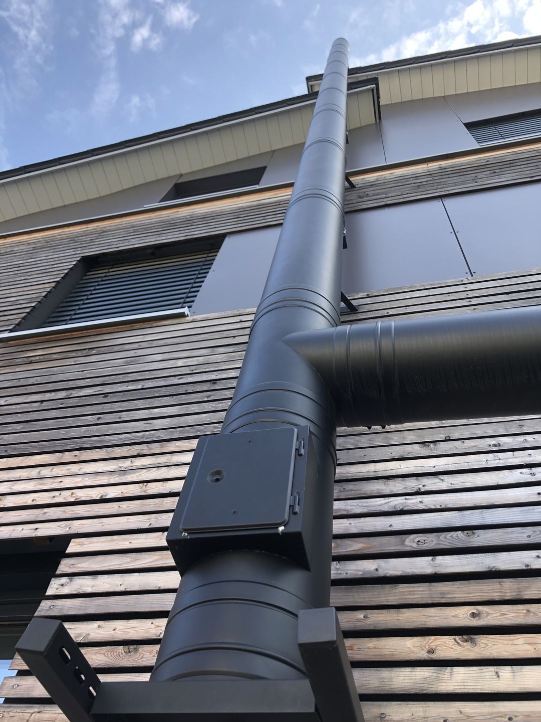 An der Seite eines Gebäudes ist ein großes schwarzes Rohr angebracht.