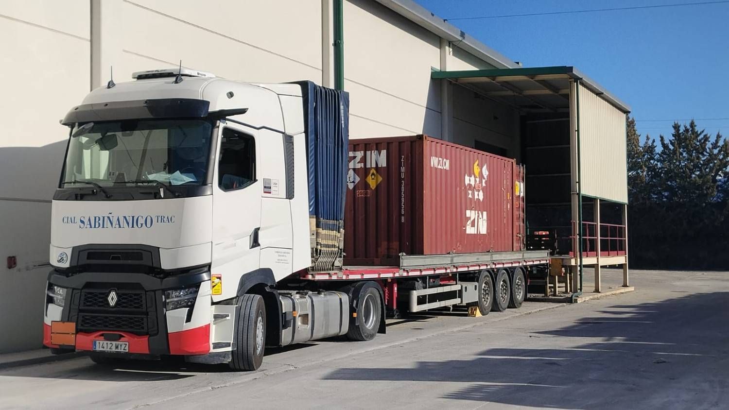 Camión cisterna con etiqueta de materiales peligrosos, estacionado cerca de una estructura roja.