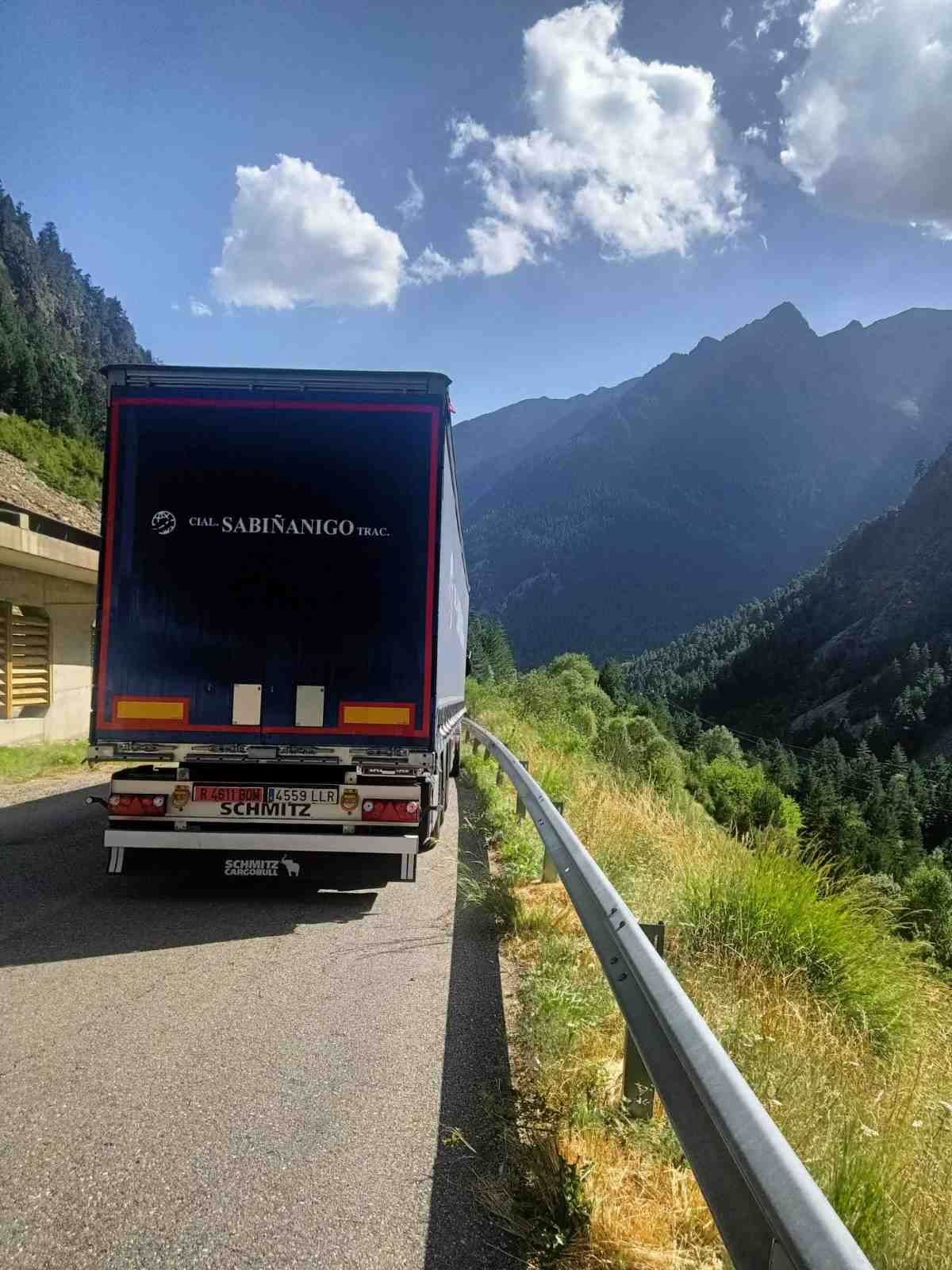 Carretera con un camión semirremolque circulando entre montañas bajo un cielo parcialmente nublado.