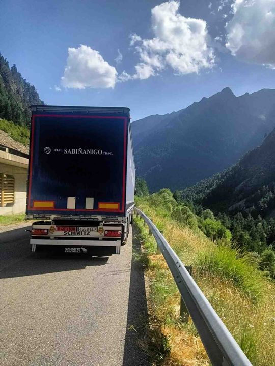 Carretera con un camión semirremolque circulando entre montañas bajo un cielo parcialmente nublado.
