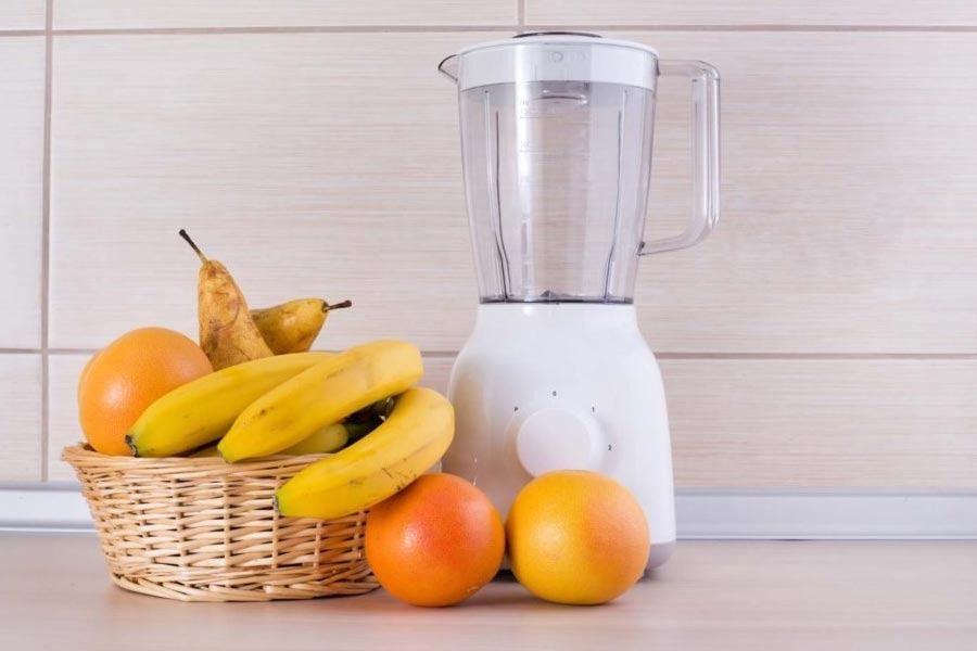 Una licuadora junto a una canasta de fruta en un mostrador.