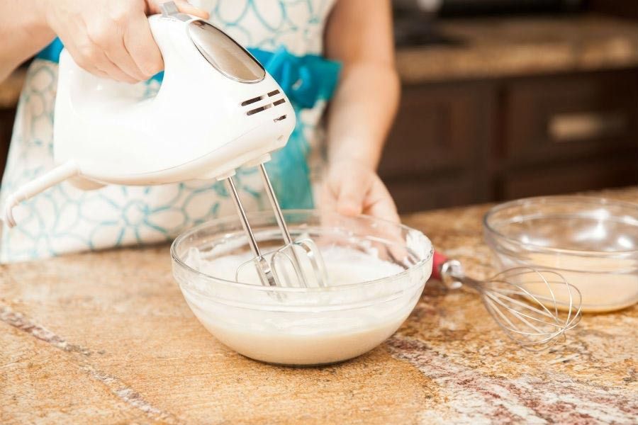 Una mujer está usando una batidora para mezclar ingredientes en un tazón.