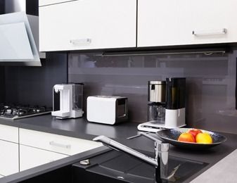 Una cocina con fregadero, horno tostador, cafetera y un bol de fruta en la encimera.
