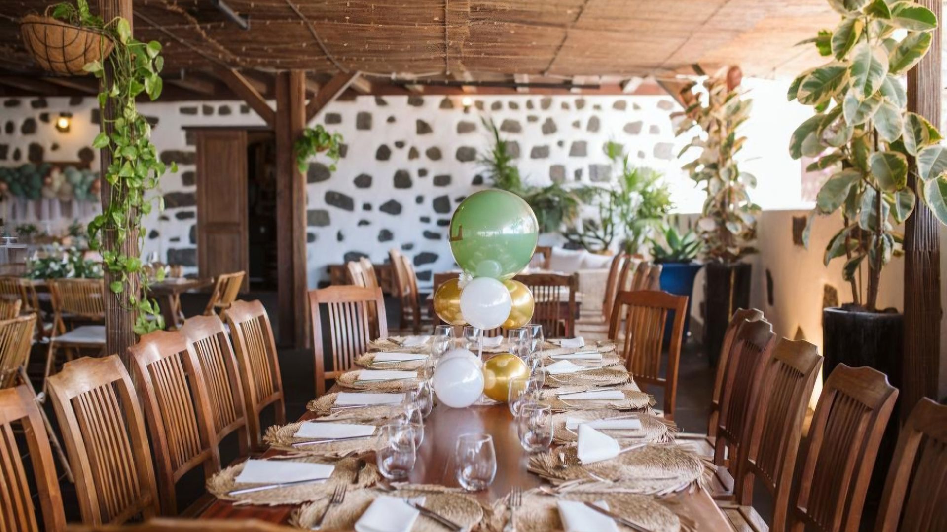Una mesa larga con platos, vasos y globos encima en un restaurante.
