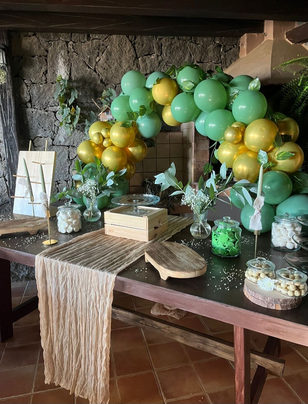 Una mesa decorada con globos verdes y dorados y dulces.