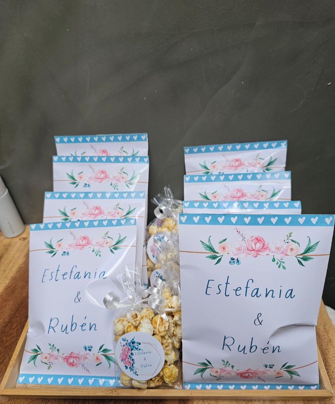 Una bandeja de madera llena de bolsas de palomitas de maíz con los nombres Estefanía y Rubén en ellas.