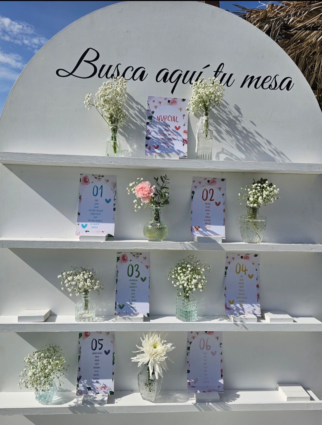 Un estante con flores y un cartel que dice busca aquí tu mesa