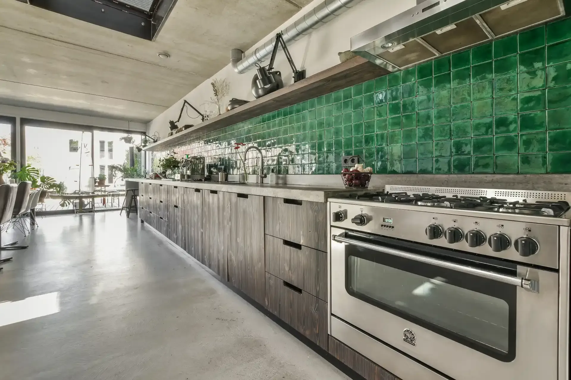 Cocina moderna con salpicadero de azulejos verdes, electrodomésticos de acero inoxidable y gabinetes de madera.