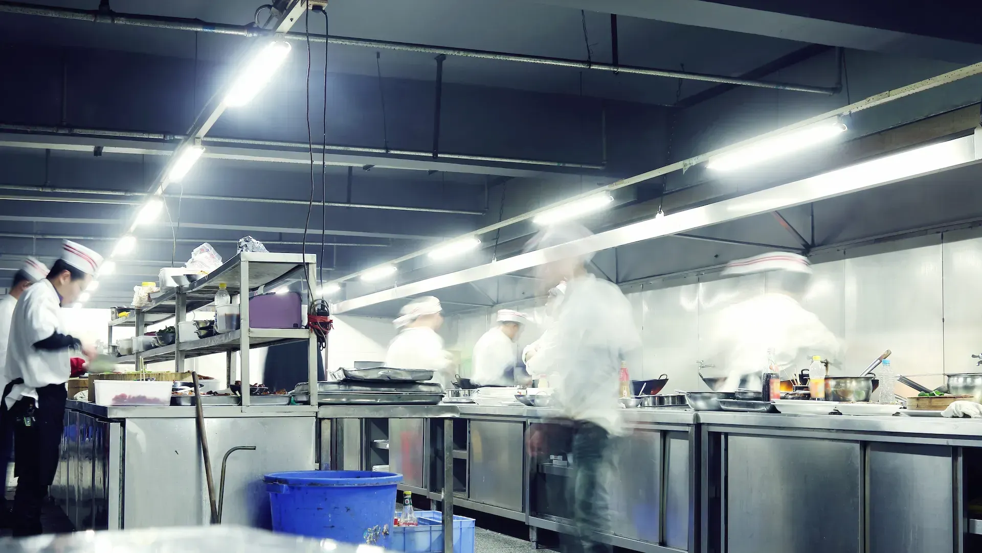 Chefs con batas blancas cocinando en una cocina industrial luminosa.