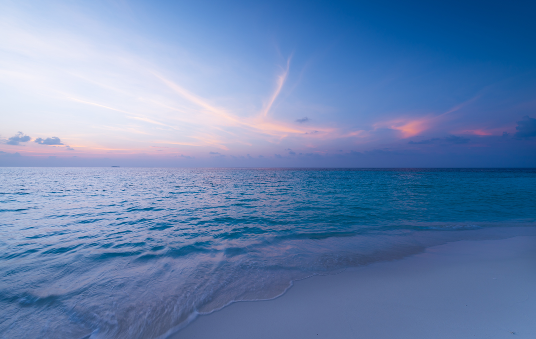 Il y a un coucher de soleil sur l'océan et une plage au premier plan.