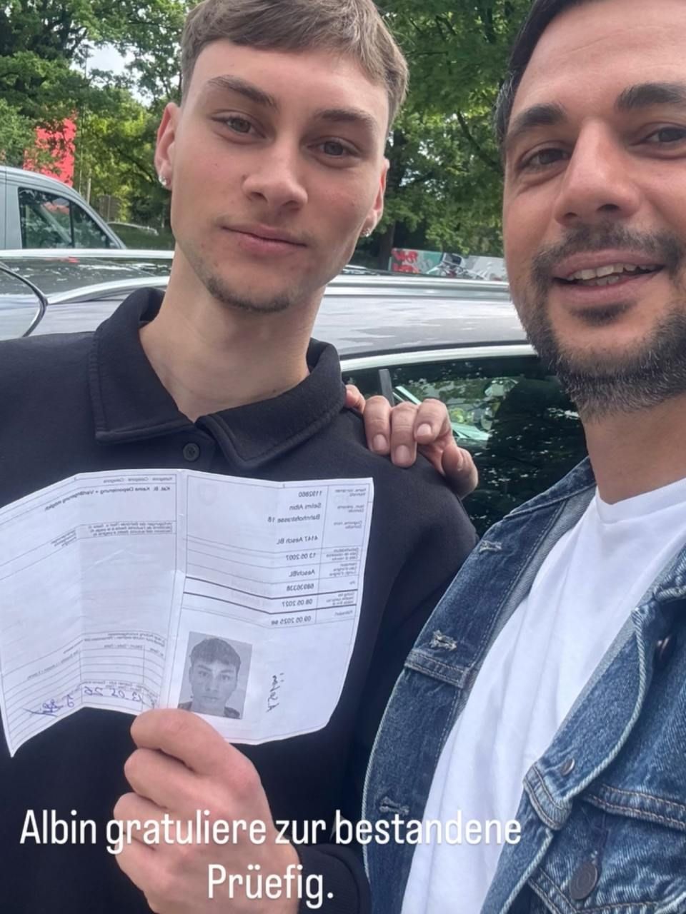 Zwei Männer posieren im Freien, einer hält ein Glückwunschschreiben in der Hand.