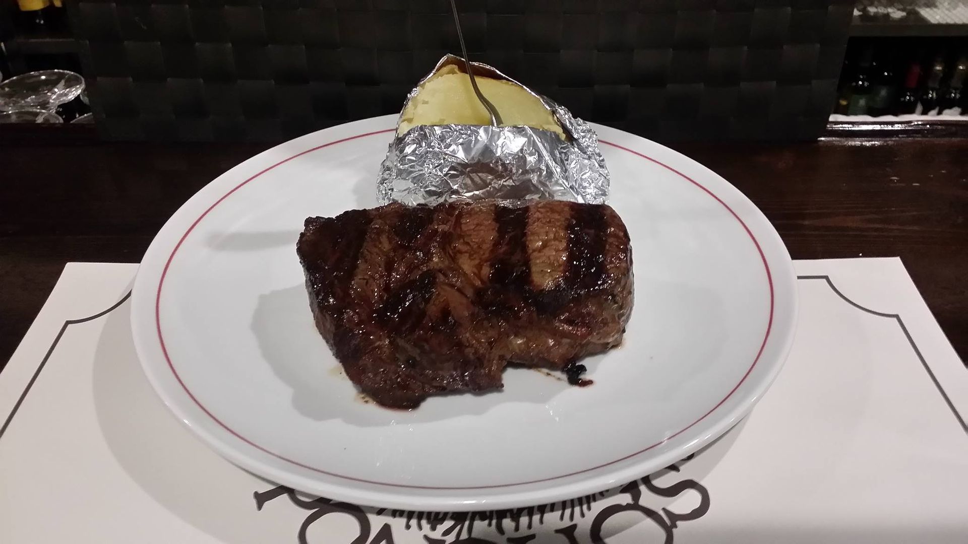 Un plato blanco con un trozo de carne y una papa al horno encima.