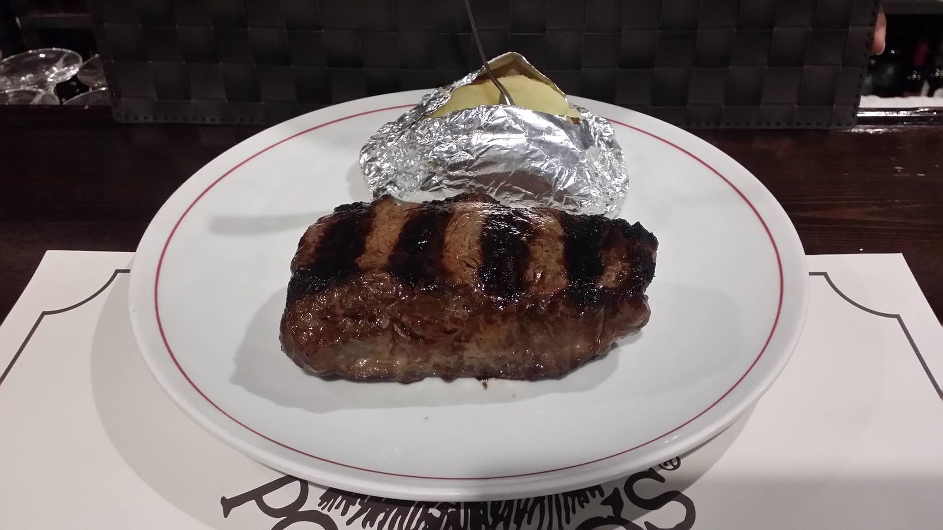 Un bistec con una papa al horno en un plato blanco