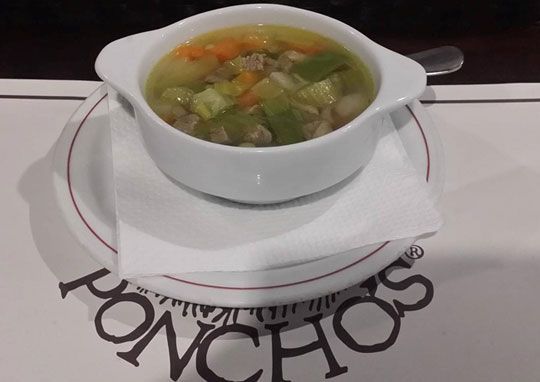 Un tazón de sopa se encuentra en un plato con la palabra poncho en él.