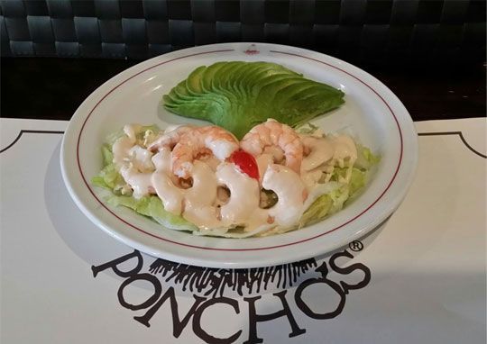 Un plato con camarones y aguacate reposa sobre un mantel de poncho.