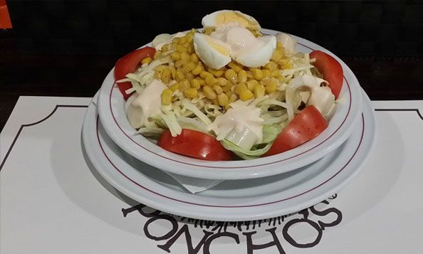 Una ensalada con tomates, maíz y huevos reposa sobre un mantel tipo poncho.