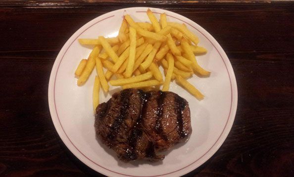 Un plato blanco cubierto con un bistec y papas fritas