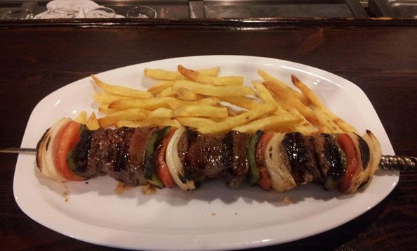 Un plato blanco cubierto con una brocheta de carne y papas fritas