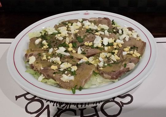Un plato blanco cubierto con carne y huevos se encuentra sobre una mesa.