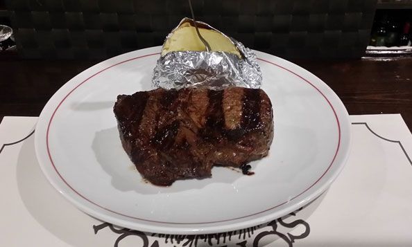 Un plato blanco cubierto con un trozo de carne y una patata asada.