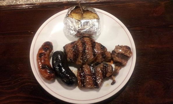 Un plato blanco cubierto con carne y patatas sobre una mesa de madera.