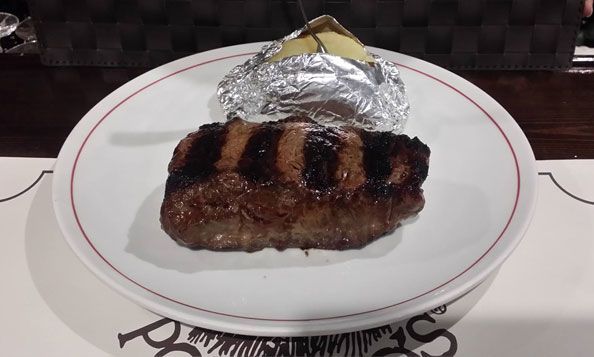 Un plato blanco cubierto con un filete y una papa al horno.
