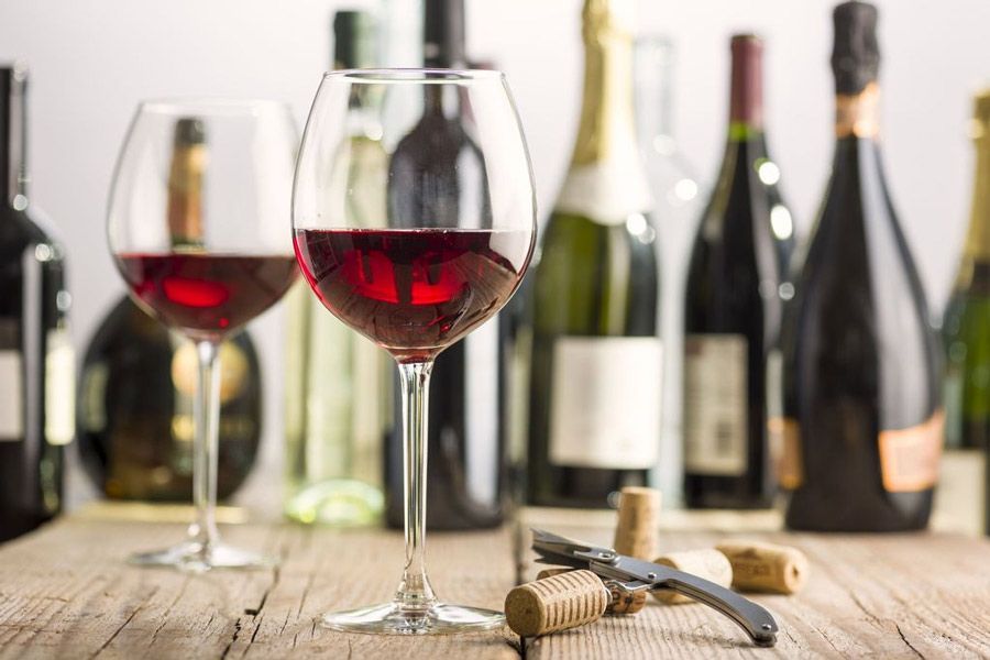 Dos copas de vino tinto están sentadas en una mesa de madera delante de botellas de vino.