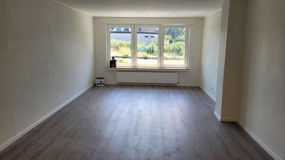 Ein leeres Wohnzimmer mit Hartholzböden und einem großen Fenster.